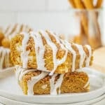 Two stacked Snickerdoodle Cookie Bars topped with white icing drizzle on a white plate.