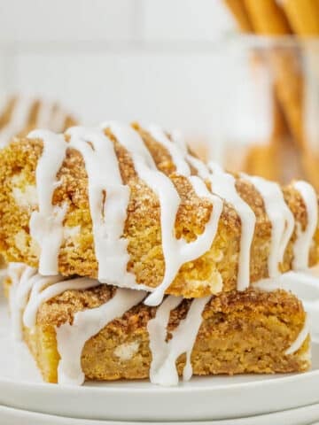 Two stacked Snickerdoodle Cookie Bars topped with white icing drizzle on a white plate.