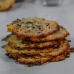 A stack of crispy, round cottage cheese chips topped with seasoning on a white counter.