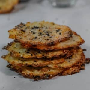 A stack of crispy, round cottage cheese chips topped with seasoning on a white counter.