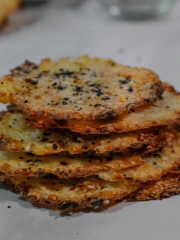 A stack of crispy, round cottage cheese chips topped with seasoning on a white counter.