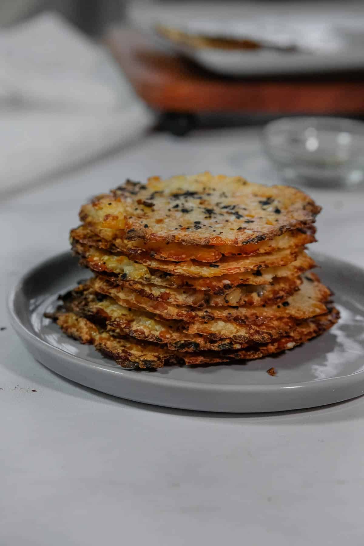 A stack of round, crispy, cottage cheese chips on a gray plate on a white surface.