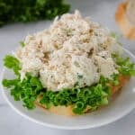Open-faced chicken salad sandwich on a slice of bread with green leaf lettuce, served on a white plate.
