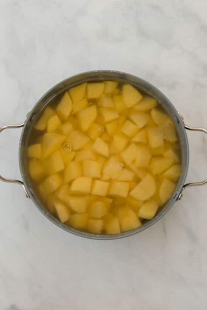 A pot filled with peeled, cubed potatoes submerged in water.