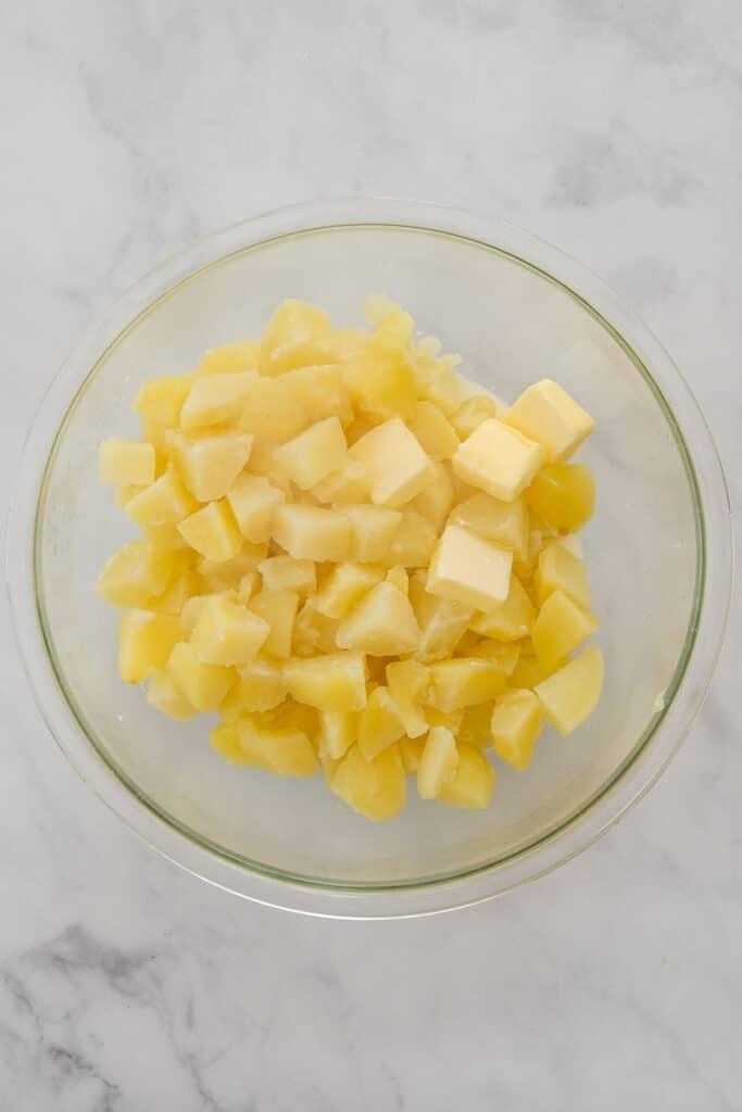 A glass bowl filled with peeled, boiled, and diced potatoes.