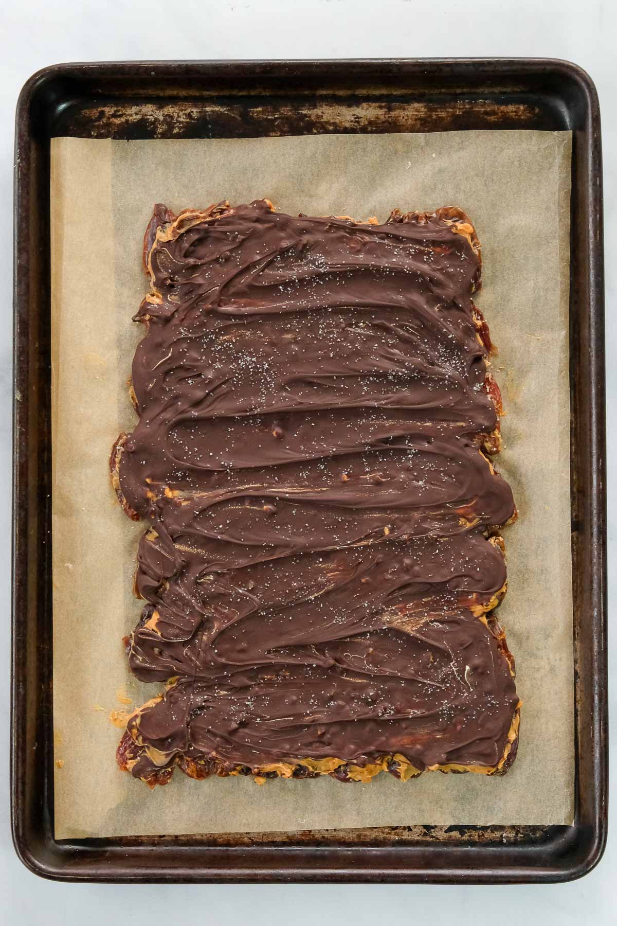 A rectangular sheet of homemade date snickers on parchment paper.