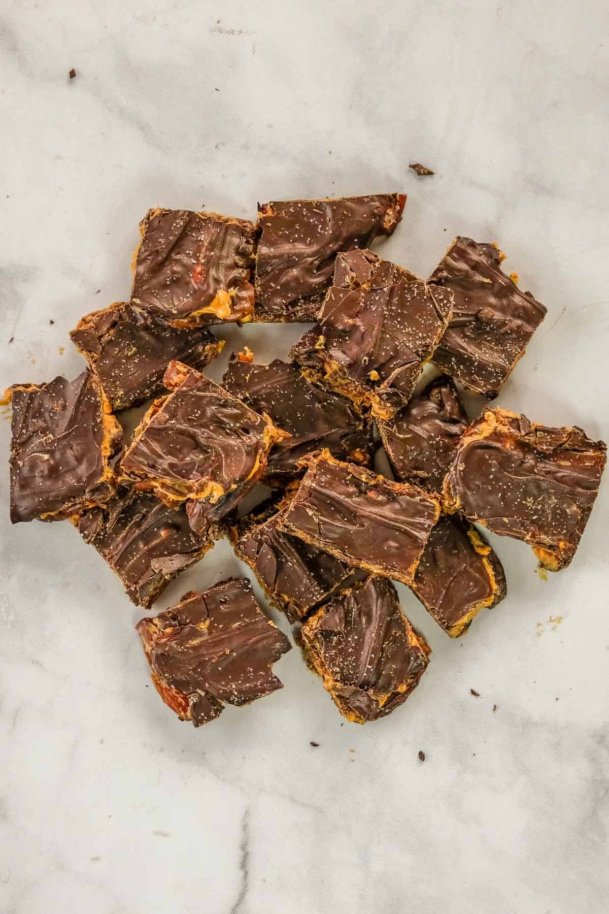 Squares of date snickers bark stacked on a white surface, with visible layers of chocolate and peanut butter and a swirl pattern on top.
