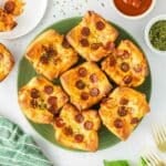 A green plate holds seven square pizza muffins with melted cheese.