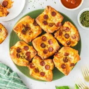 A green plate holds seven square pizza muffins with melted cheese.