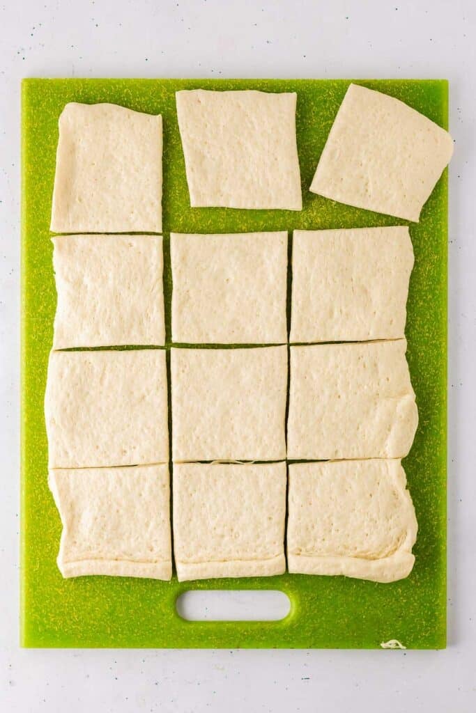 Rectangular pieces of raw dough are arranged on a green cutting board.