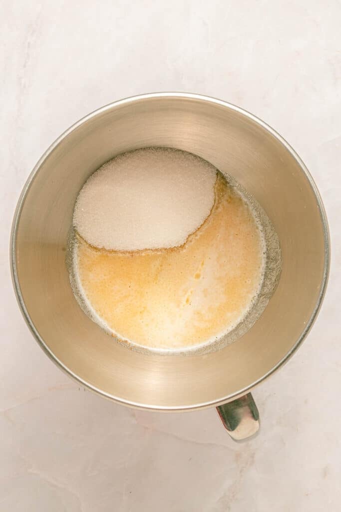 A metal mixing bowl containing beaten eggs and granulated sugar on a light countertop.