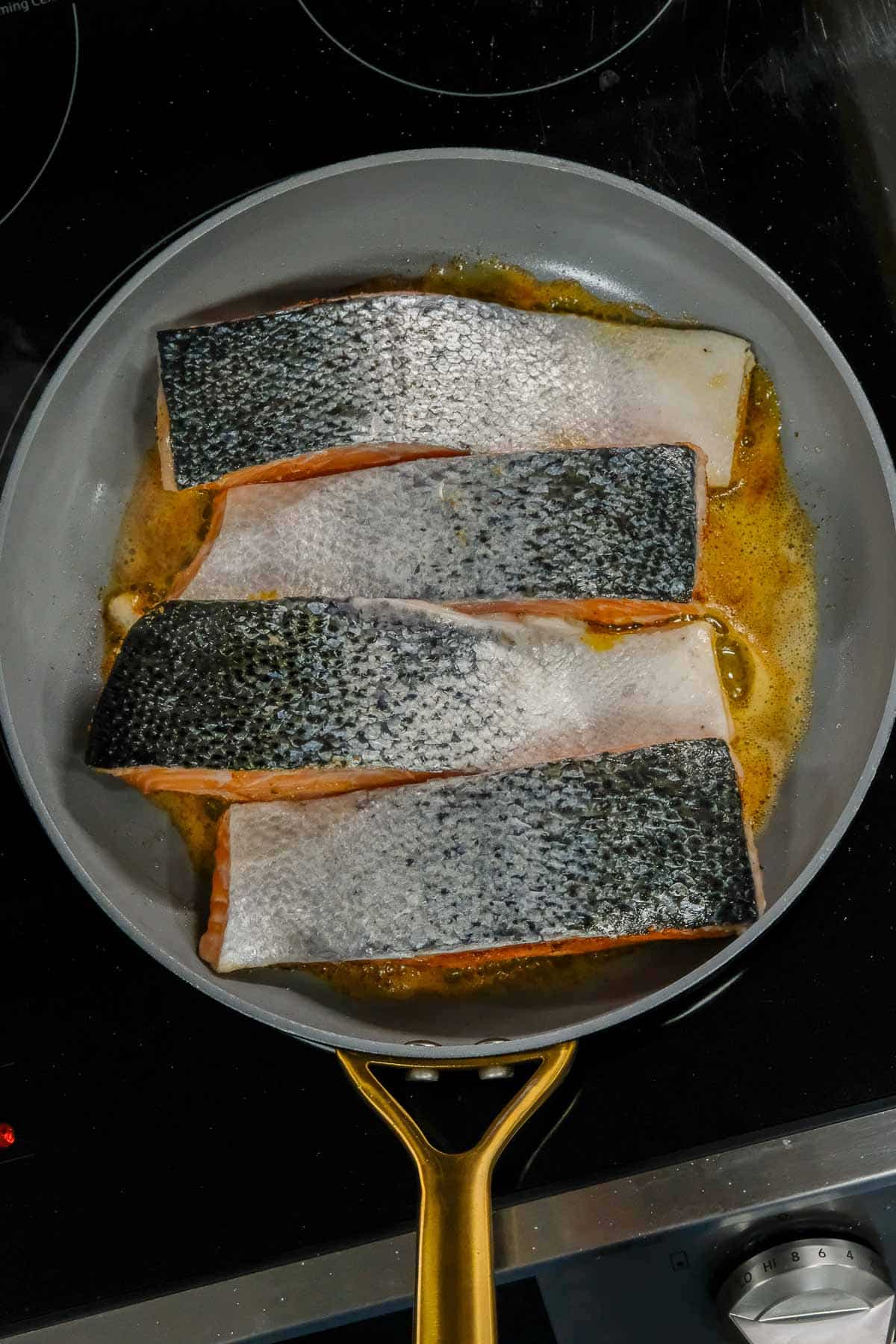 Salmon fillets cooking in a frying pan with oil on a stovetop.