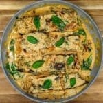 Tuscan salmon fillets in a creamy sauce with spinach, sun-dried tomatoes, and basil leaves in a skillet, viewed from above.