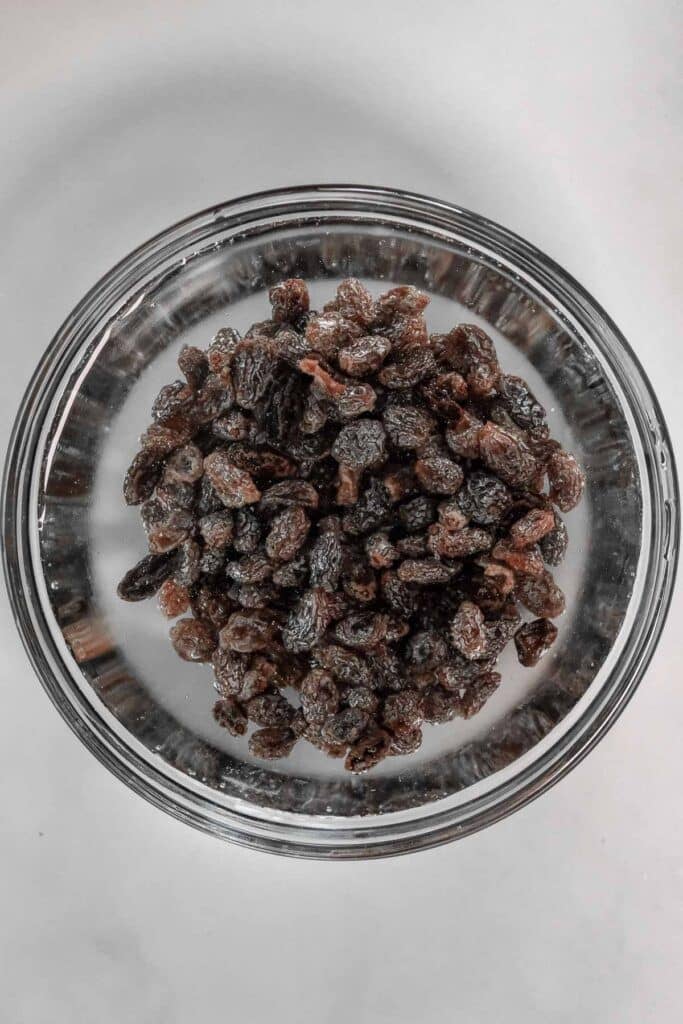 A bowl filled with raisins placed on a light colored surface.
