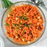 A glass bowl filled with carrot salad mixed with chickpeas, raisins, and chopped green onions.
