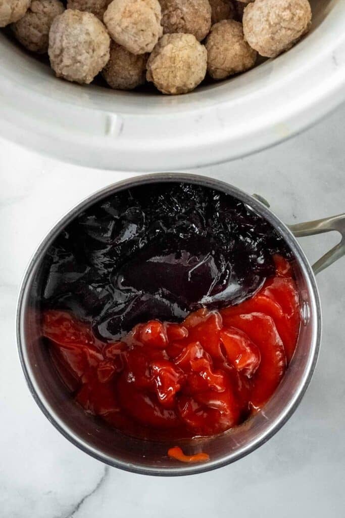 A pot containing grape jelly and ketchup sits next to a slow cooker filled with frozen meatballs.