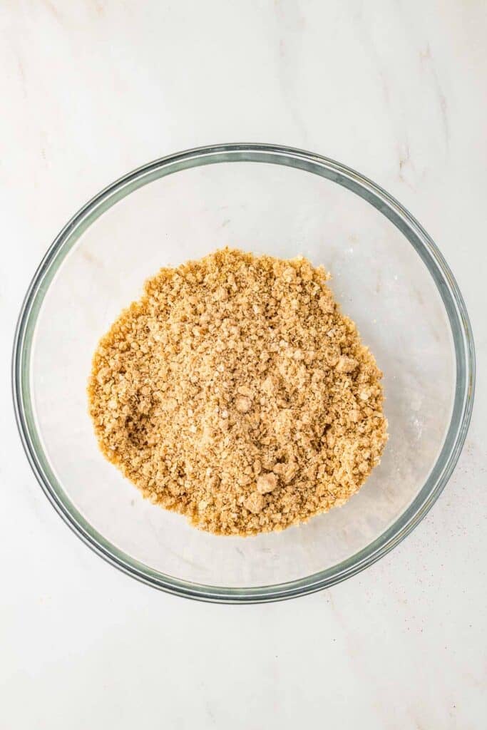 A clear glass bowl containing a cinnamon sugar crumble topping on a light-colored surface.
