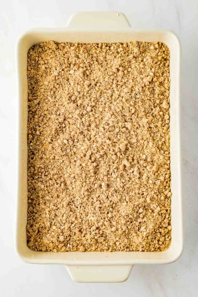 Rectangular baking dish filled with an even layer of uncooked, crumbly oat and flour mixture, likely prepared for baking a crisp or crumble dessert.