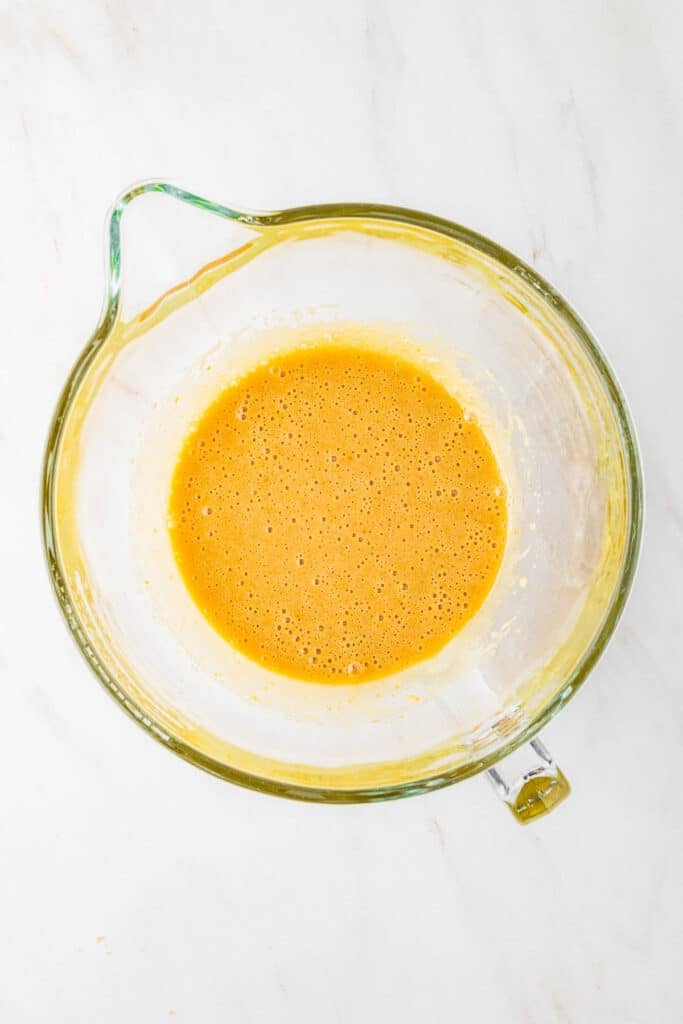 A glass mixing bowl containing a whisked egg mixture on a white marble surface.