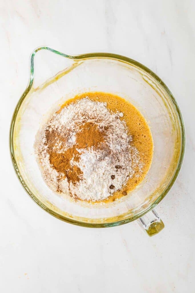 A glass mixing bowl with an egg mixture with flour, baking soda, cinnamon, and nutmeg added in.
