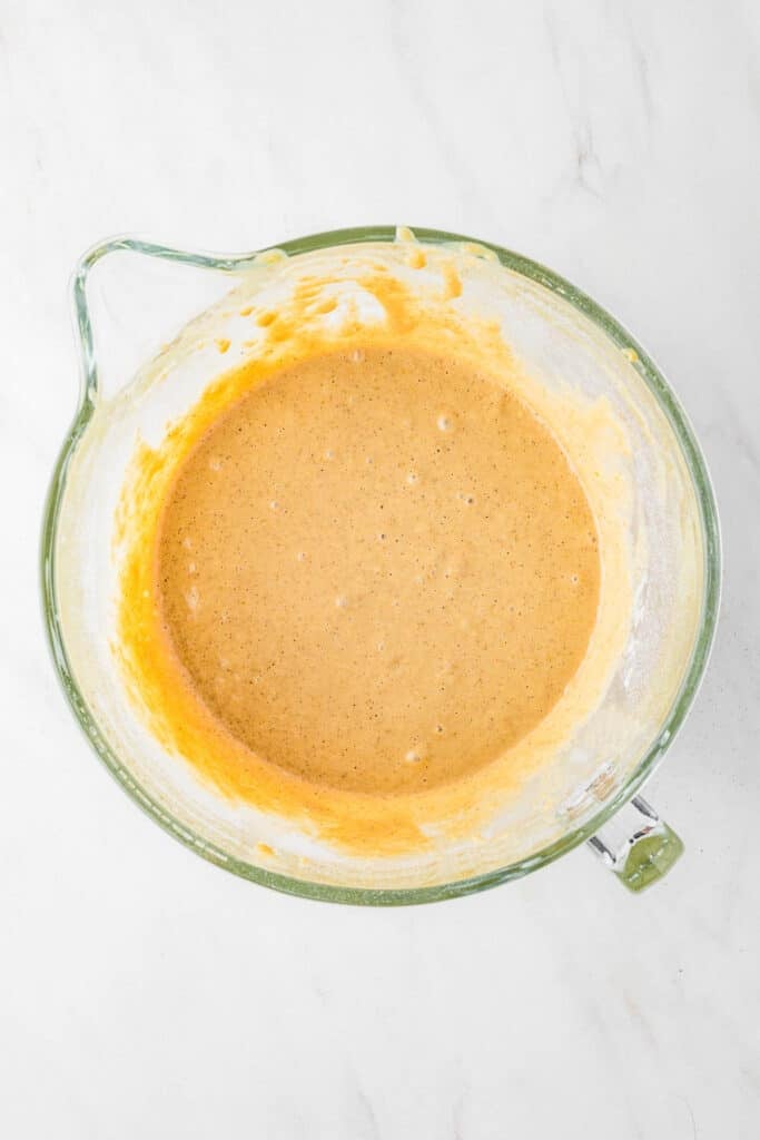 Glass mixing bowl containing Applesauce Crumb Cake batter on a white marble surface.