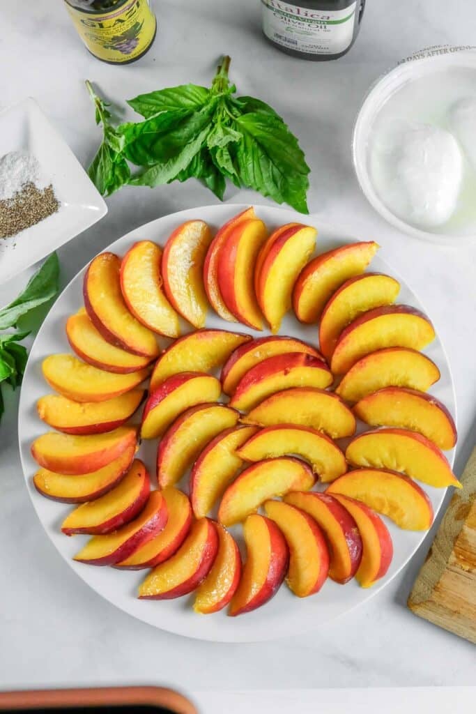 A white plate with neatly arranged slices of fresh yellow peaches.