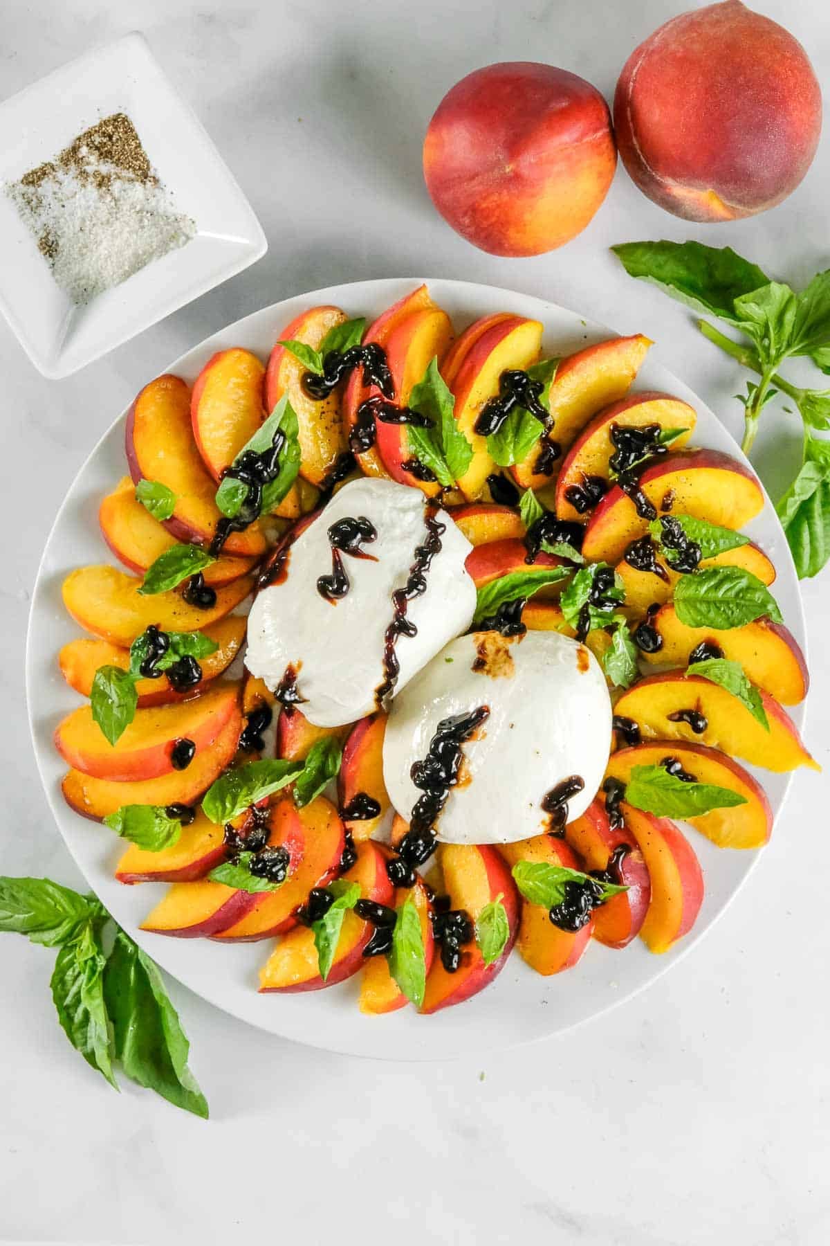 A plate with sliced peaches, fresh burrata, basil leaves, and balsamic glaze.