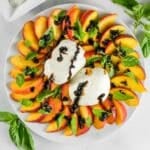 A plate with sliced peaches, fresh burrata, basil leaves, and balsamic glaze.
