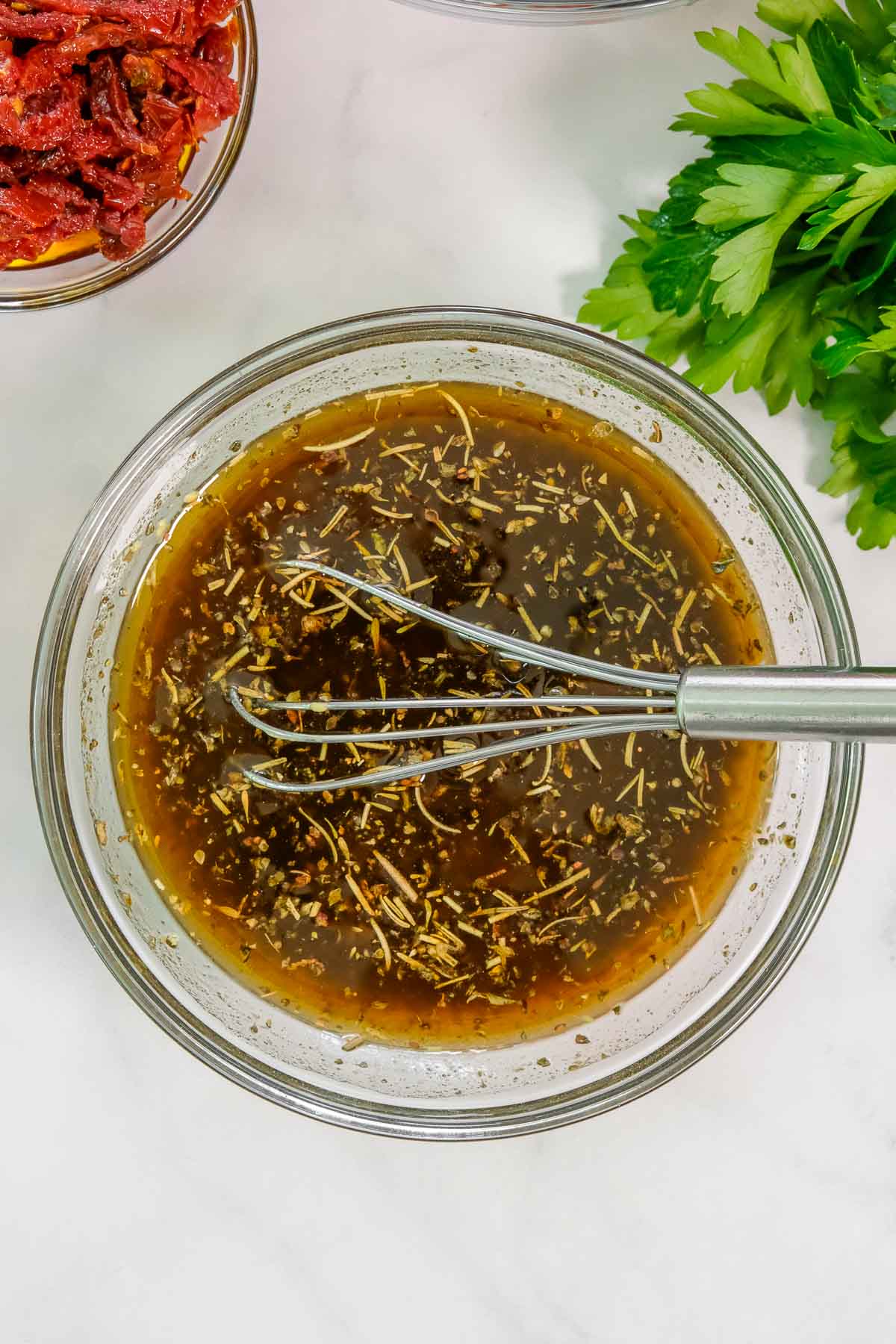 A metal whisk rests in a glass bowl filled with dressing ingredients for marinade.