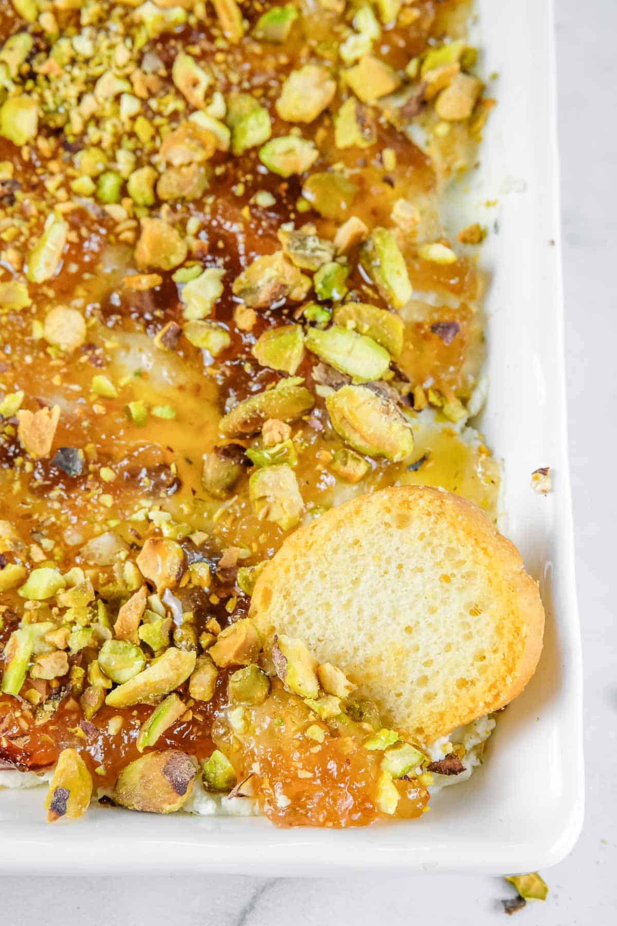 A close-up of a rectangular white dish of Boursin cheese dip topped with chopped pistachios.