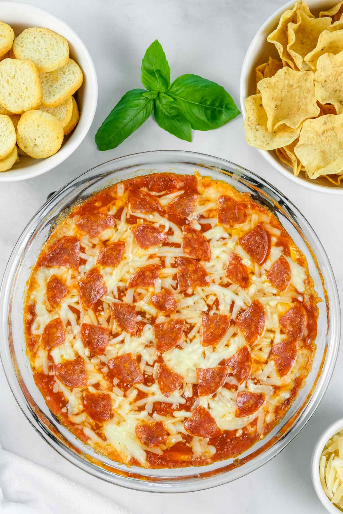 Glass dish of baked pizza dip topped with melted cheese and pepperoni slices.
