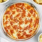 Glass dish of baked pizza dip topped with melted cheese and pepperoni slices.