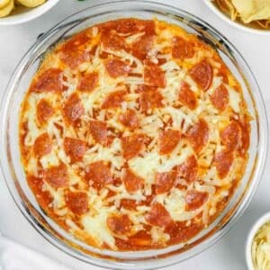 Glass dish of baked pizza dip topped with melted cheese and pepperoni slices.