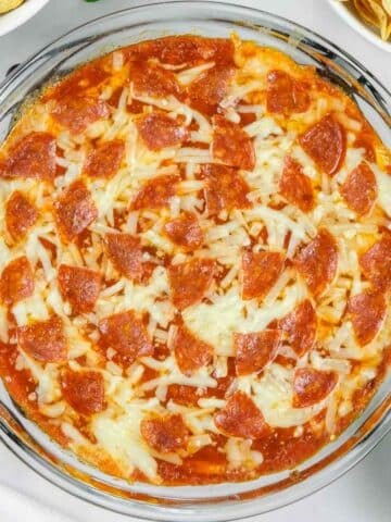 Glass dish of baked pizza dip topped with melted cheese and pepperoni slices.