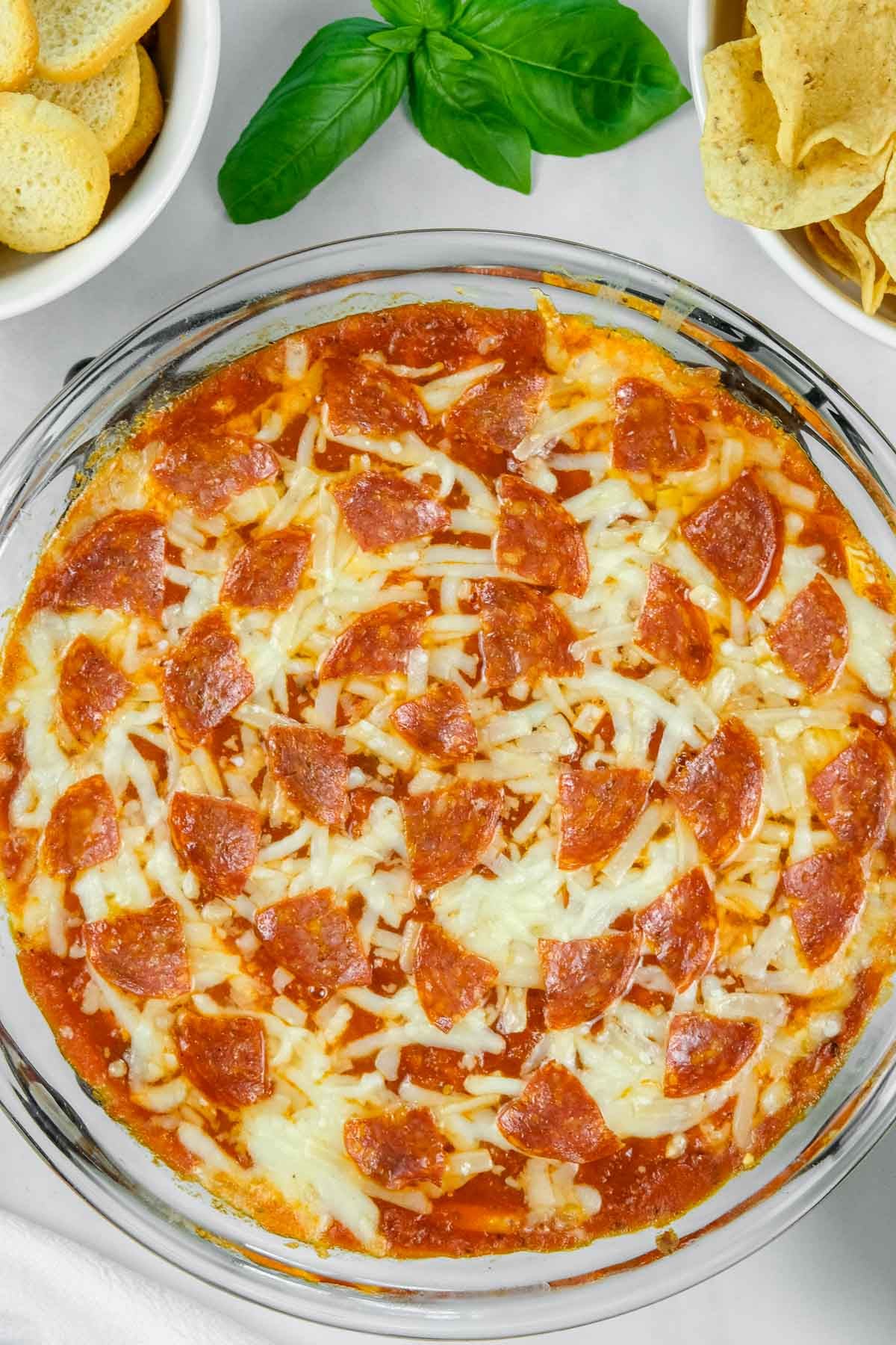 Glass dish of baked pizza dip topped with melted cheese and pepperoni slices.