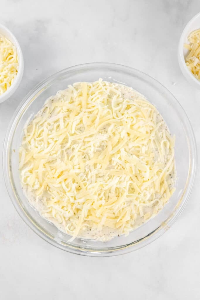 A glass dish filled with a creamy mixture topped with shredded cheese.