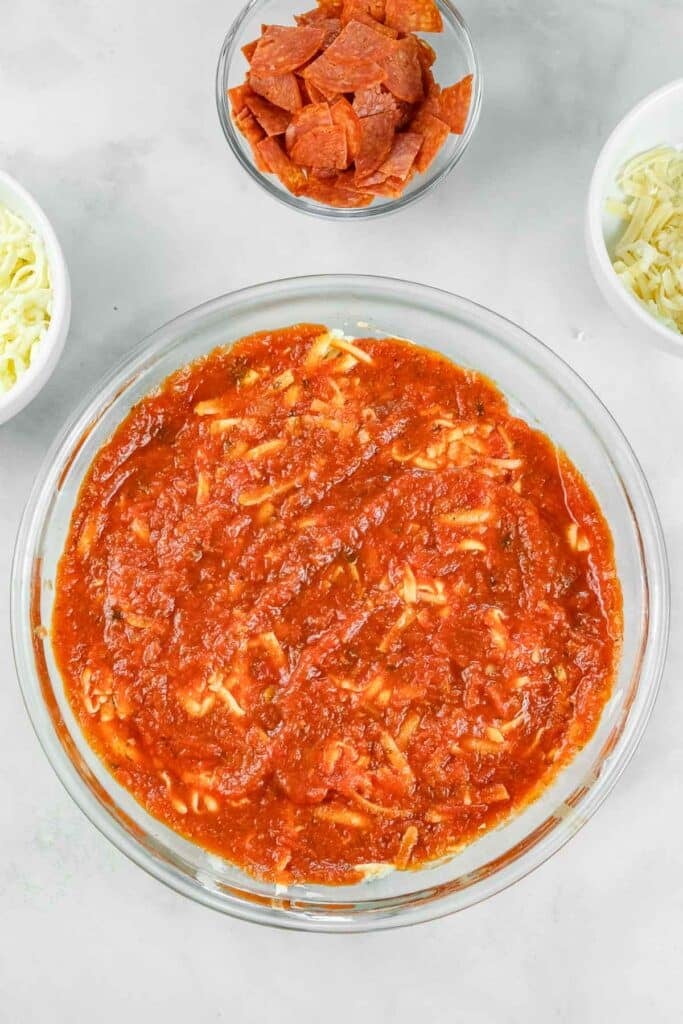 A glass dish filled with cream cheese mix, tomato sauce, and cheese.