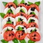 Easy Caprese salad recipe with slices of tomato and mozzarella arranged with basil leaves, topped with balsamic glaze on a white plate.