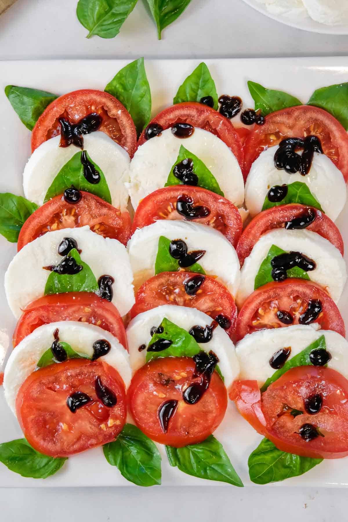 Slices of tomato, mozzarella, and basil leaves are arranged on a plate, drizzled with balsamic glaze.