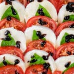 Caprese salad with sliced tomatoes, fresh mozzarella, basil leaves, and balsamic glaze arranged in rows on a white plate.