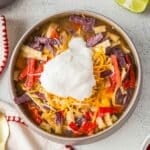 A bowl of chicken tortilla soup topped with shredded cheese, tortilla strips, and a dollop of sour cream.