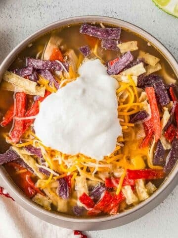 A bowl of chicken tortilla soup topped with shredded cheese, tortilla strips, and a dollop of sour cream.