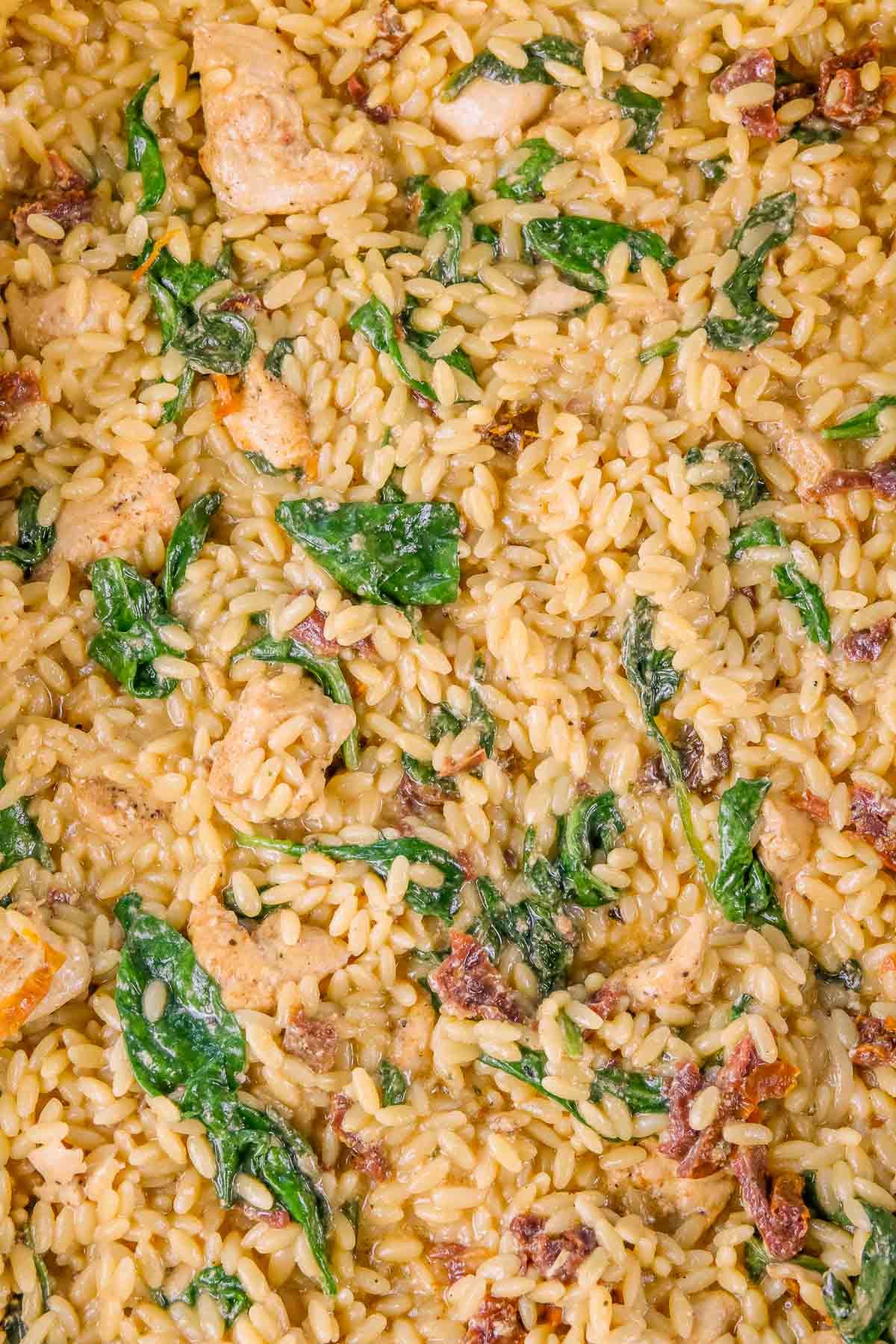 Close-up of baked chicken orzo with pieces of chicken, spinach, and bits of sun-dried tomato, all mixed together in a single dish.