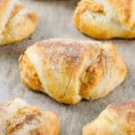 A close-up of Pumpkin Cream Cheese Crescent Rolls with a dusting of cinnamon sugar on a baking sheet.
