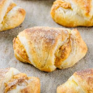 A close-up of Pumpkin Cream Cheese Crescent Rolls with a dusting of cinnamon sugar on a baking sheet.