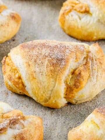 A close-up of Pumpkin Cream Cheese Crescent Rolls with a dusting of cinnamon sugar on a baking sheet.