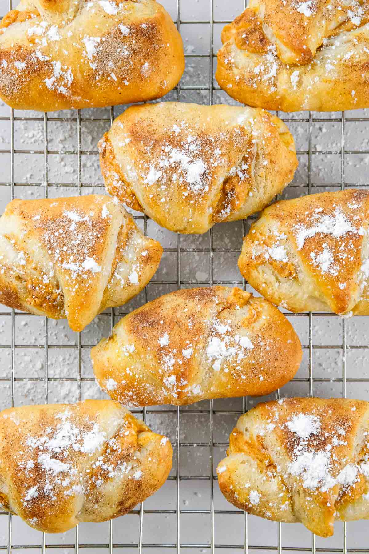 Eight Pumpkin Cream Cheese Crescent Rolls dusted with powdered sugar are arranged on a wire cooling rack.
