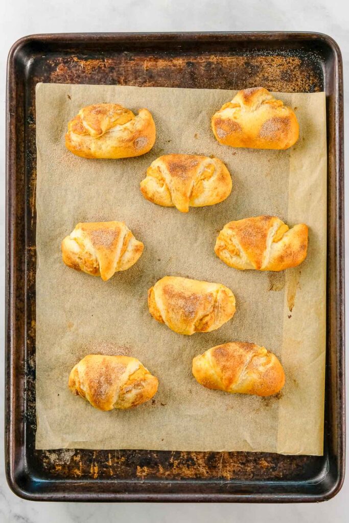 Nine baked crescent rolls on a parchment-lined baking sheet, viewed from above on a light surface.