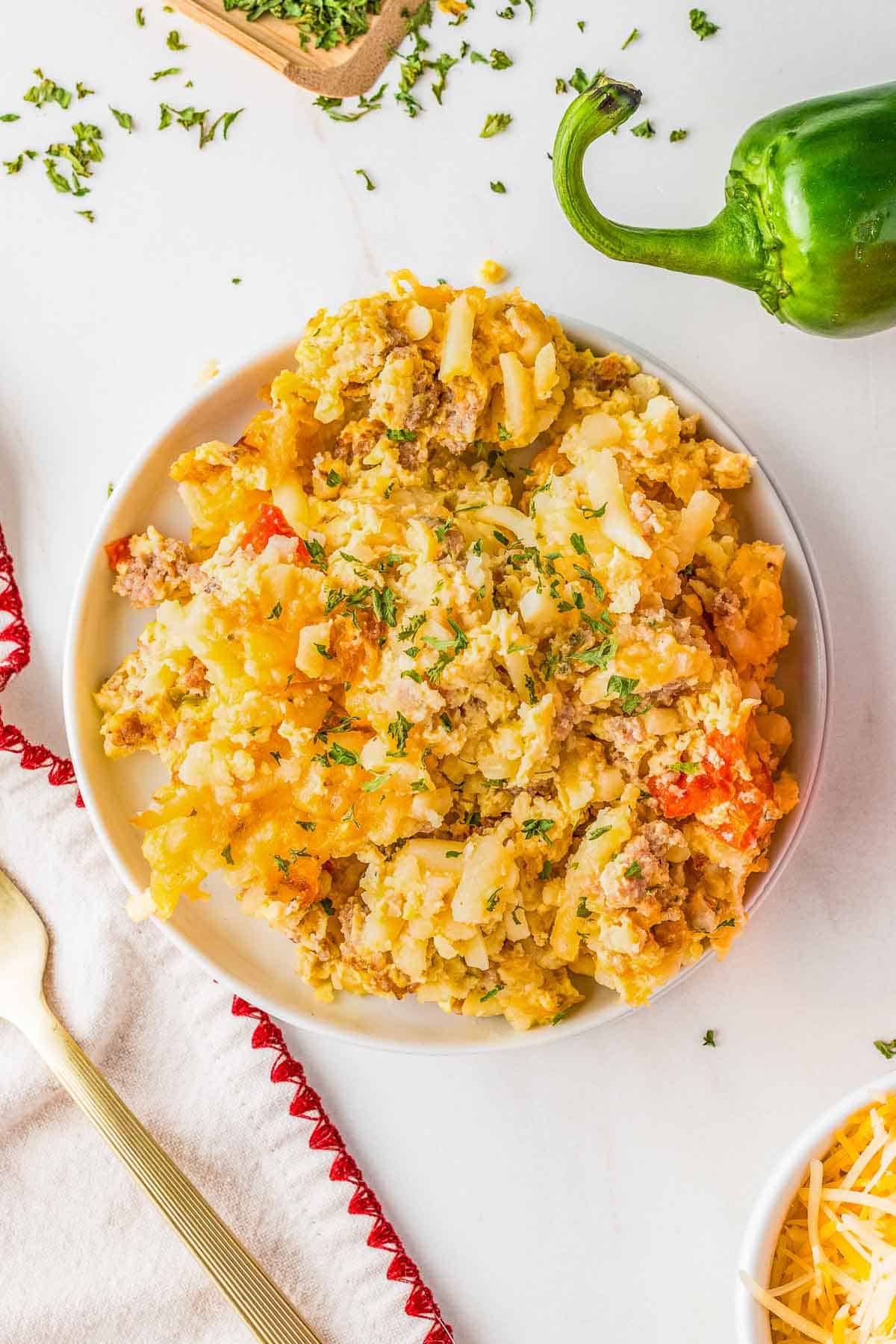 A white plate with a serving of cheesy hash brown casserole containing ground meat and red peppers, garnished with chopped herbs.