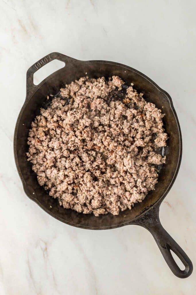 Cooked ground meat in a black cast iron skillet sits on a light-colored marble surface.